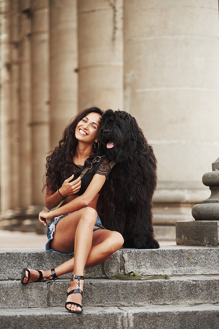 Dog owner. Beautiful woman with curly black hair have good time in the city at daytime.