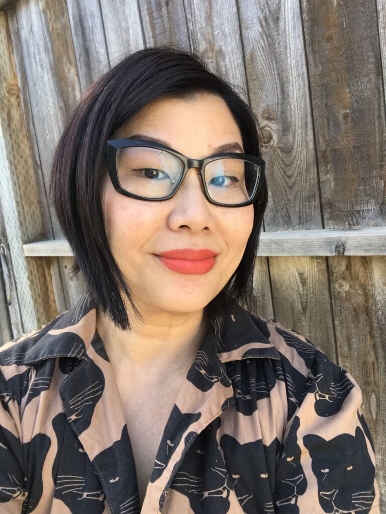 An asian woman in glasses in front of a fence.