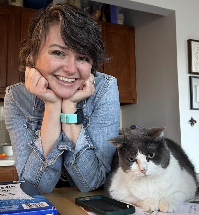 A woman posing next to a grey and white cat.
