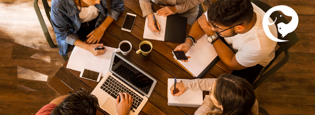A table with coffee, books, notebooks, and laptops, all being used by people sitting together.