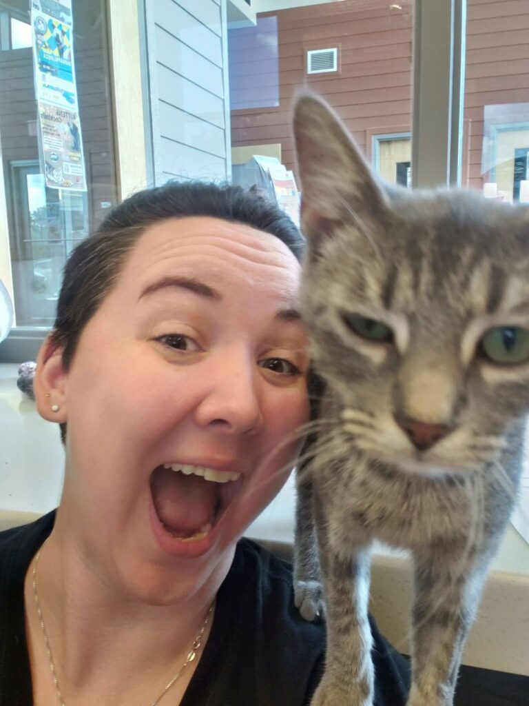 A woman smiling with a cat on her shoulder.