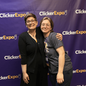 Two white women with their arms around each other standing in front of a purple ClickerExpo background.