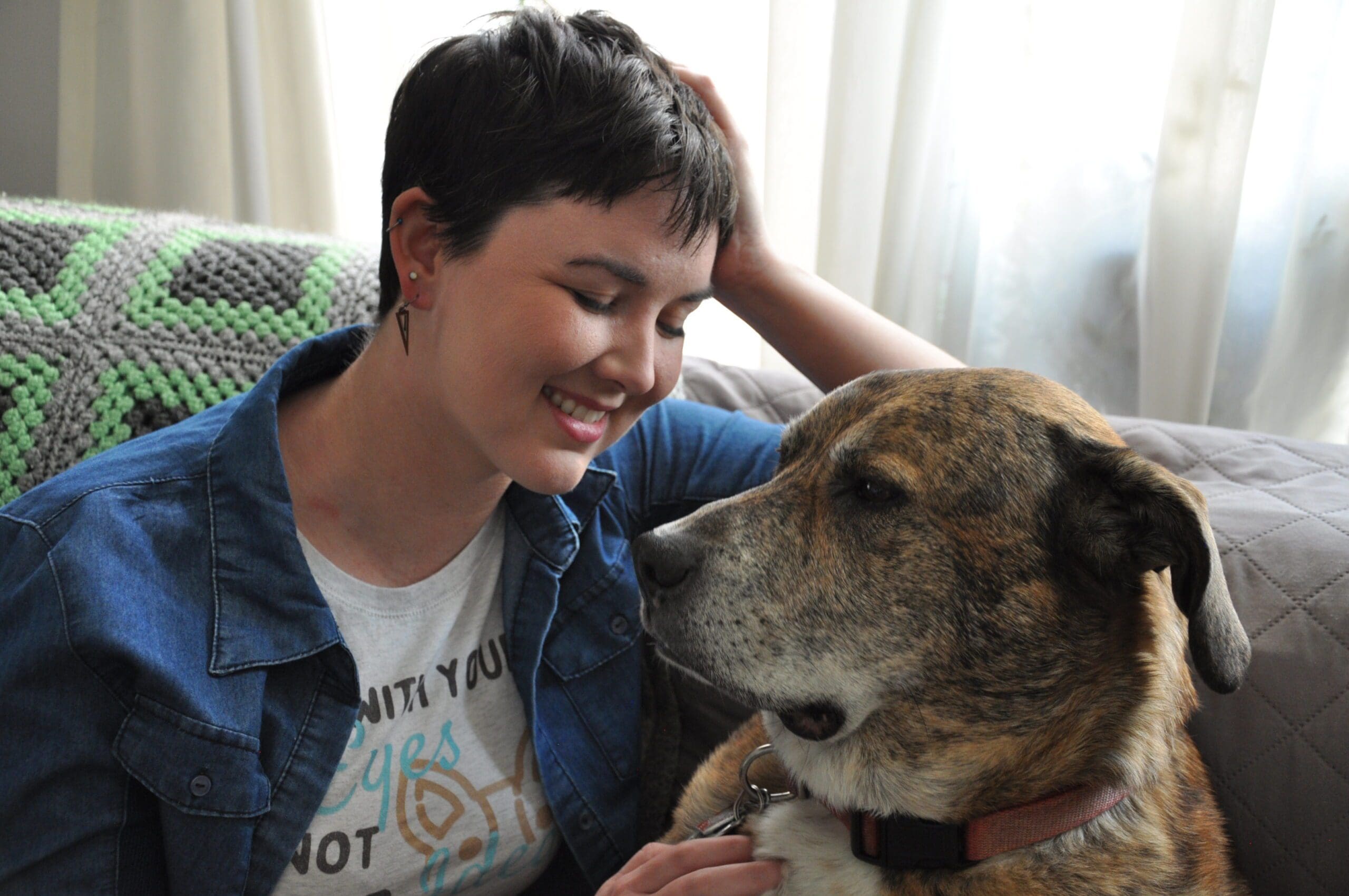 A woman sitting next to a brindle dog on a couch. Allie Bender CDBC, CPDT-KA, dog trainer mentor.