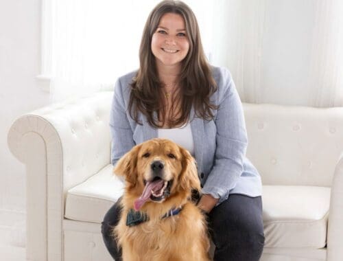 A woman with long brown hair sitting on a white couch in an all white room with a golden retriever in front of her. Juliana Dewillems on why management is enrichment.
