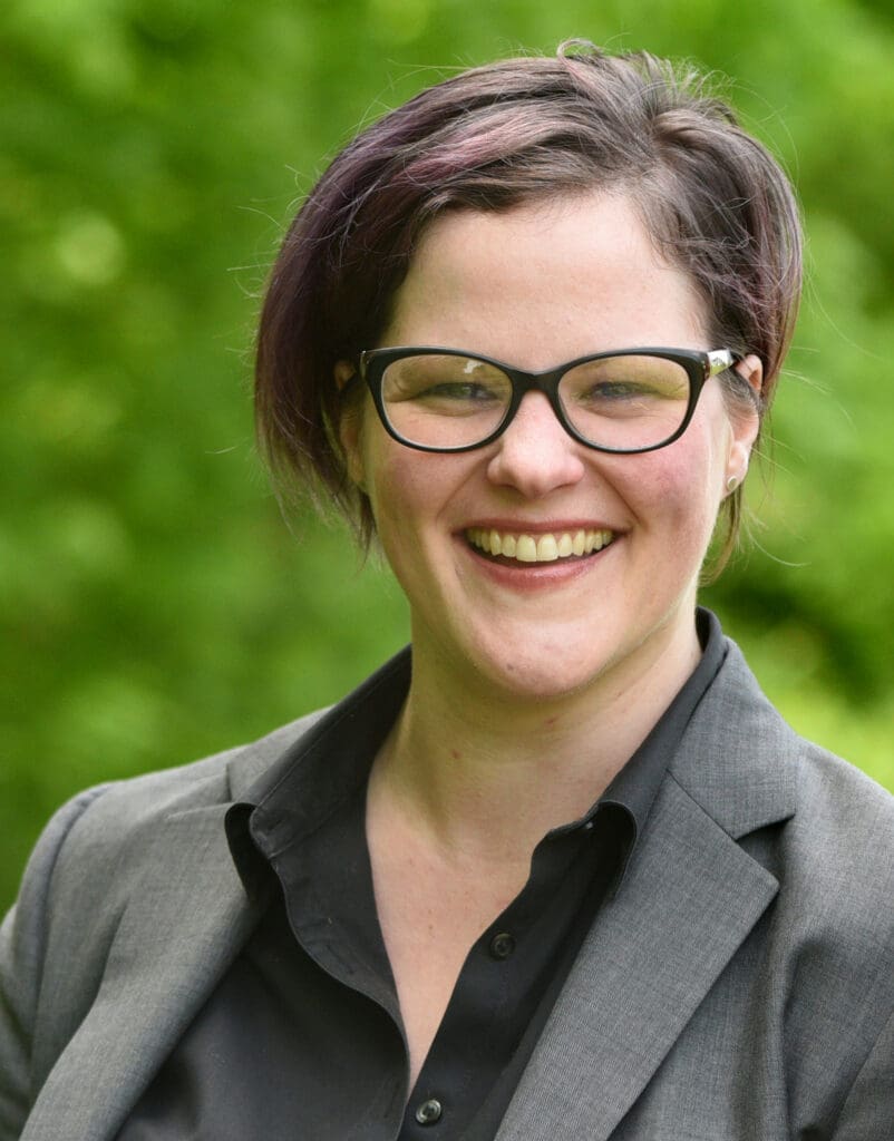 Headshot of a short-haired woman with glasses in a grey suit.