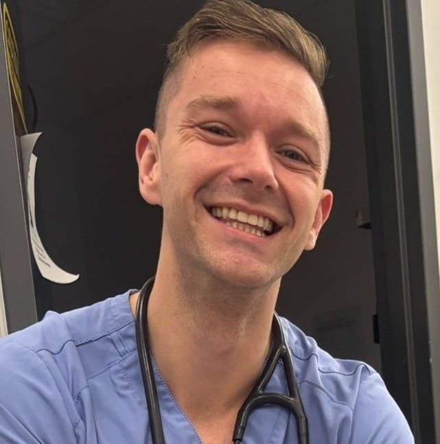 Dr. Andy smiling in blue scrubs with a stethoscope around his neck.