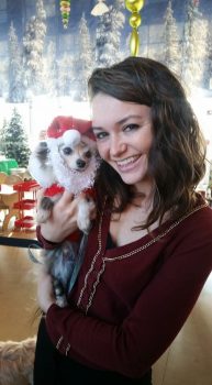 A woman holding a small dog in a santa outfit.