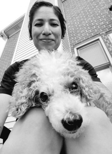 Woman with dark hair and a toy poodle in her lap looking down into the camera. Veronica Garcia, CVT and force-free dog behavior consultant at Pet Harmony, with her dog Dash.