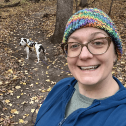 A woman in a brightly colored knit hat in the woods with her dog. Tiffany Holmes, CPDT-KA.